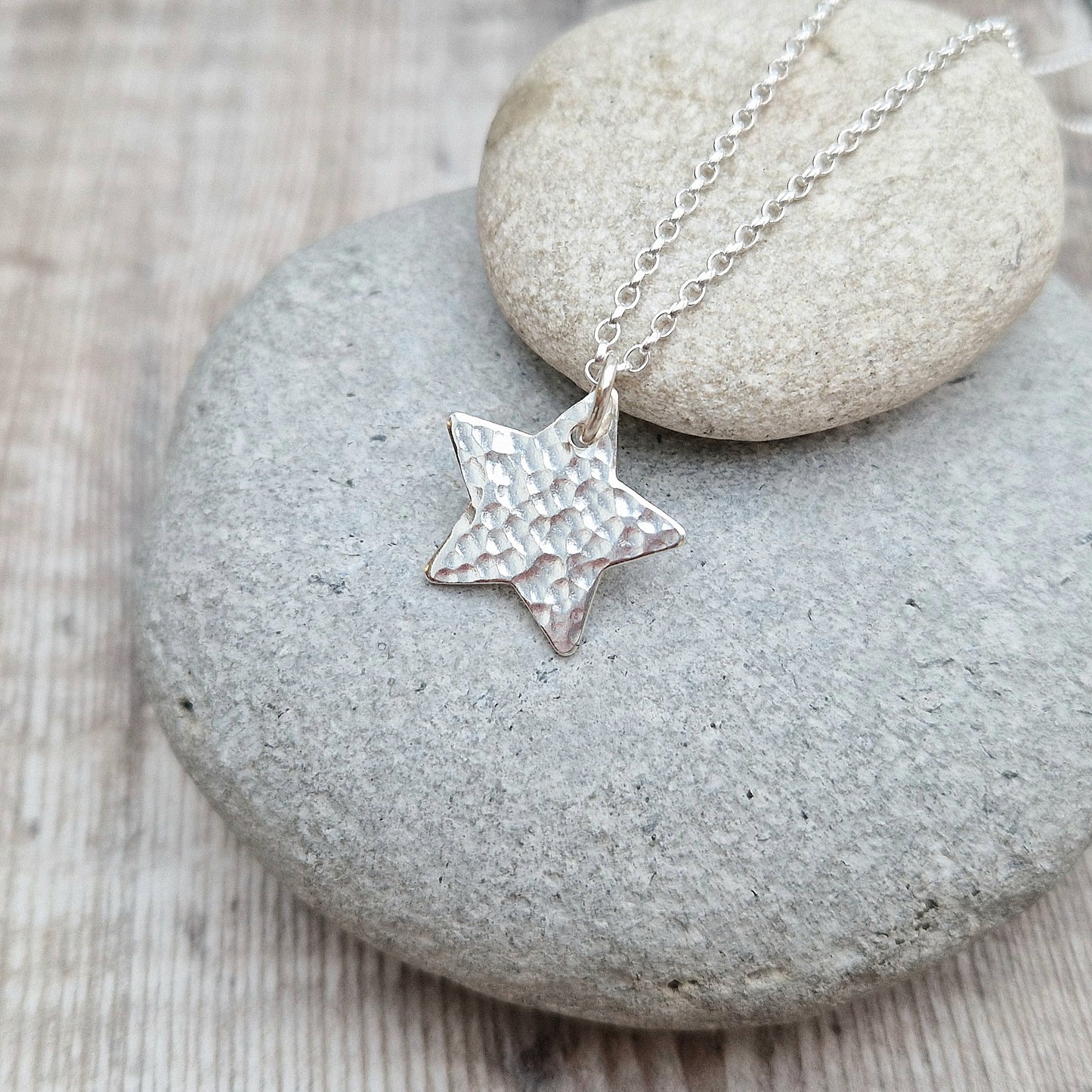 Pendant is a silver five-pointed flat star shape with hammered texture finish suspended from silver chain via a small open circle link.