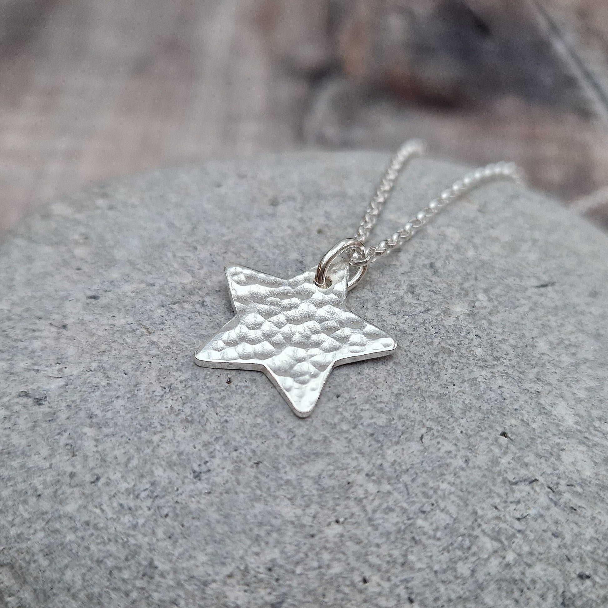 Pendant is a silver five-pointed flat star shape with hammered texture finish suspended from silver chain via a small open circle link.