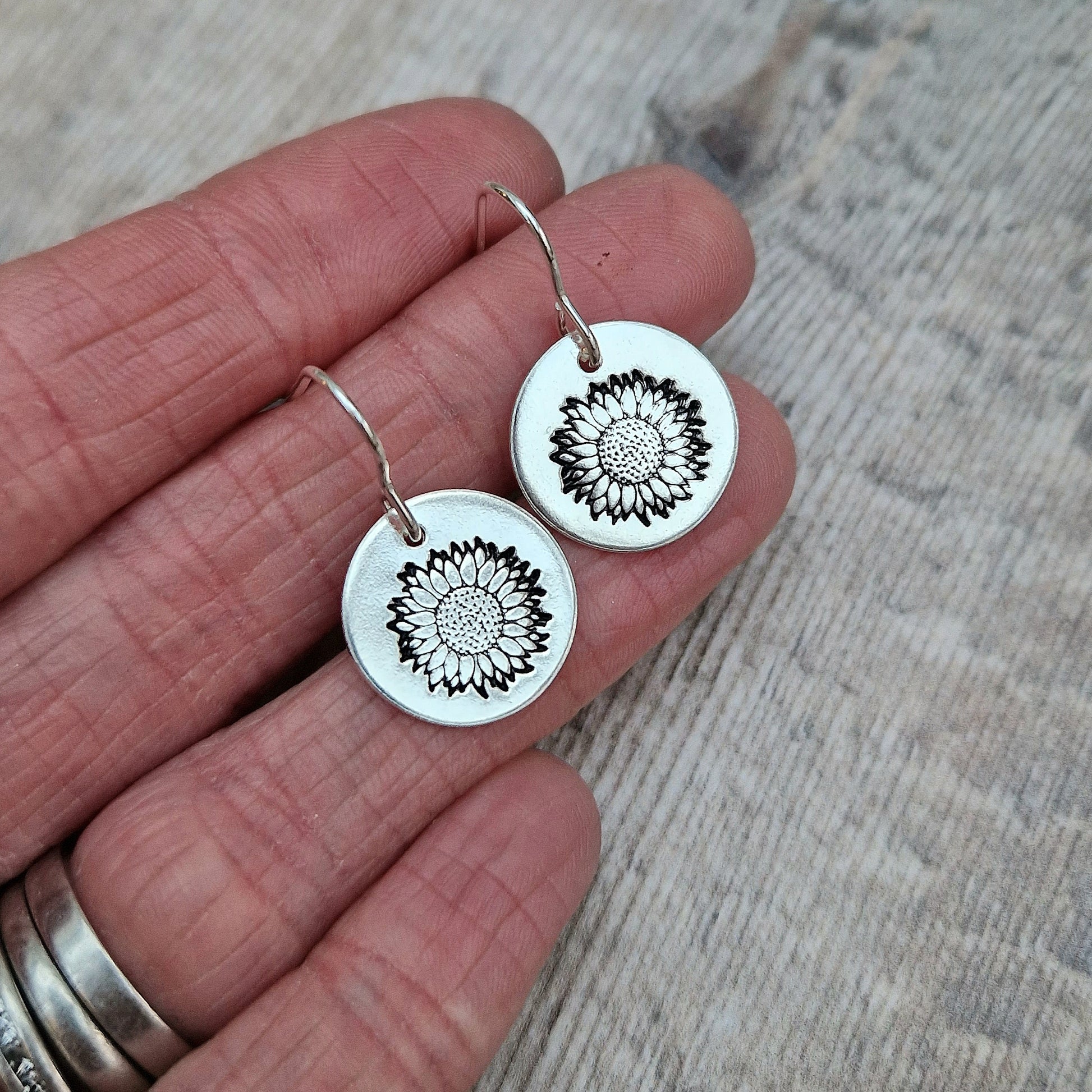 Each earring is a Sterling Silver disc suspended from silver earring wire. Each disc is stamped with a sunflower image.