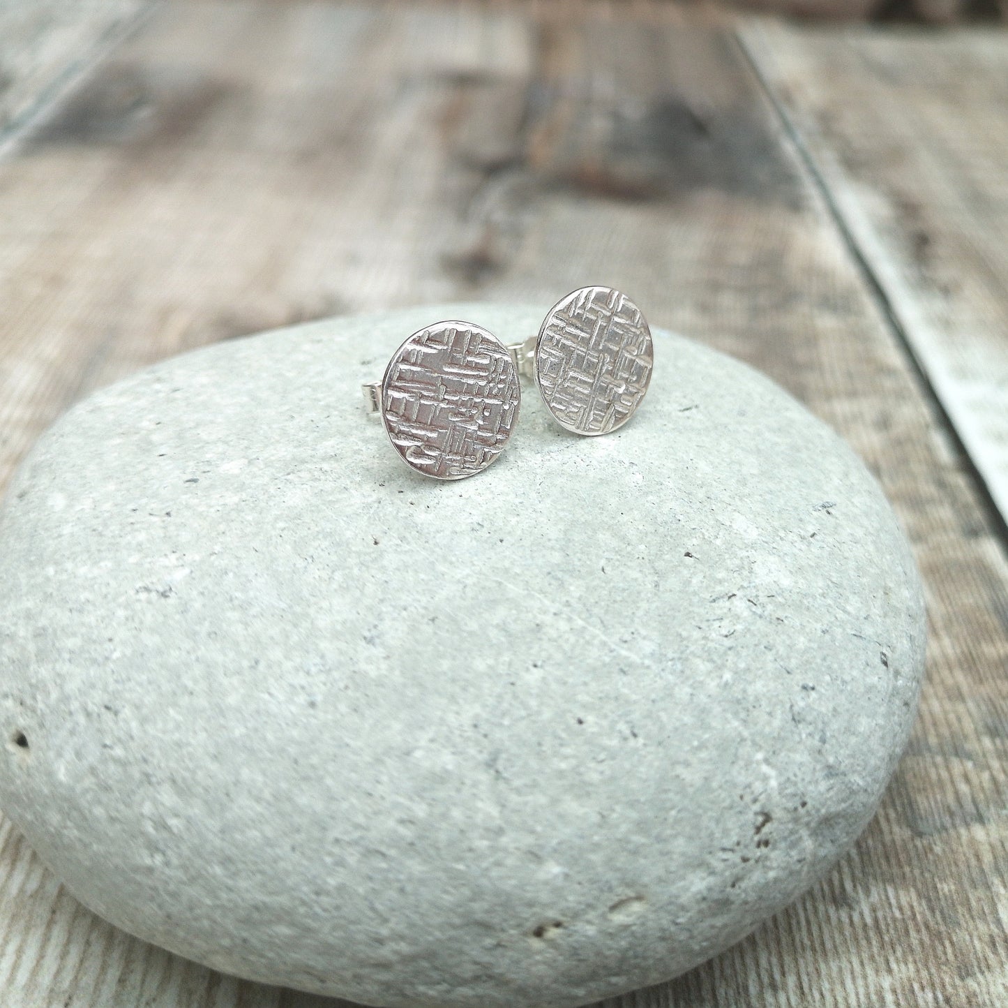 Each earring is a silver round disc stamped with irregular lines and to add a textured finish. Mounted on a silver stud bar.